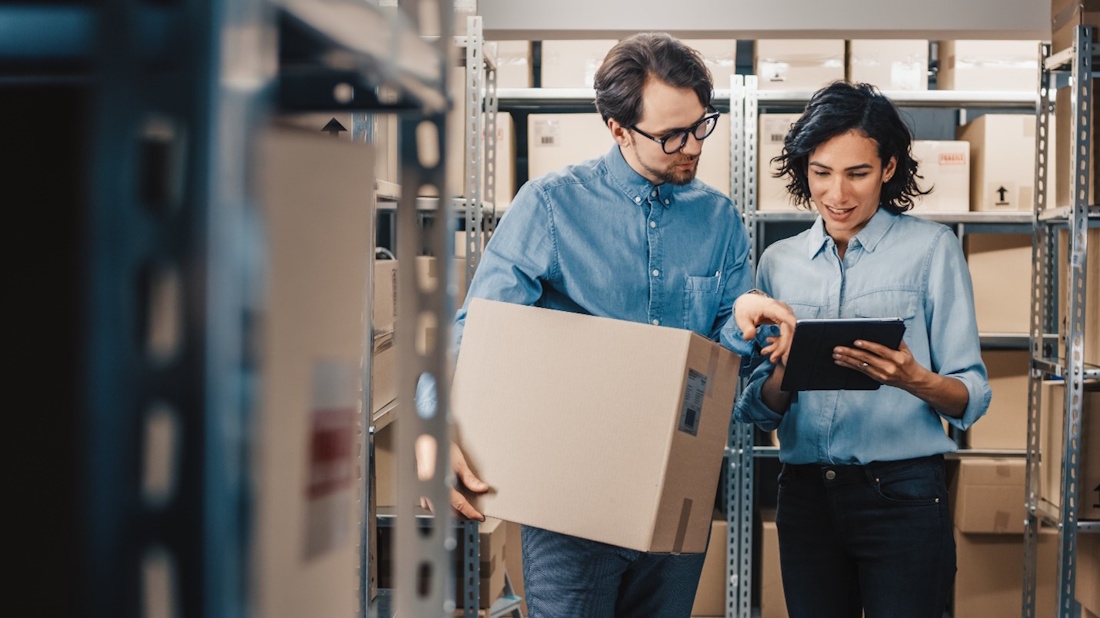 man holding a box and woman walking through a warehouse