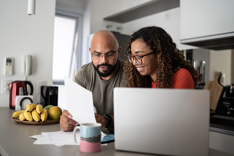 Couple smiling sitting at kitchen counter looking at documents.