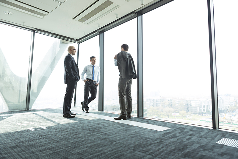 Three men in suits standing in empty office space in high rise building