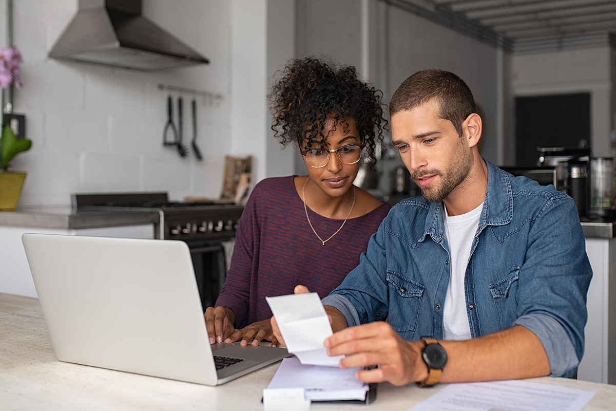 Couple sitting at kitchen table looking at bills and laptop