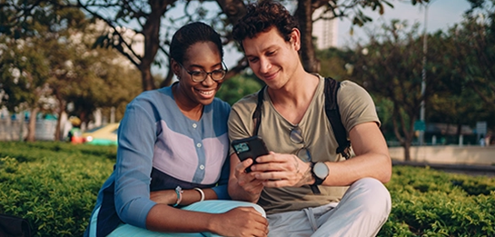 two university students sitting on park bench looking at phone