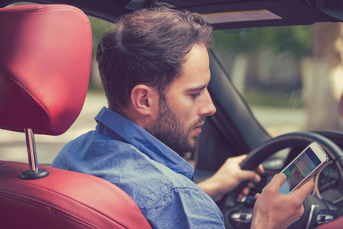 Man looking down at cell phone in car with red seats