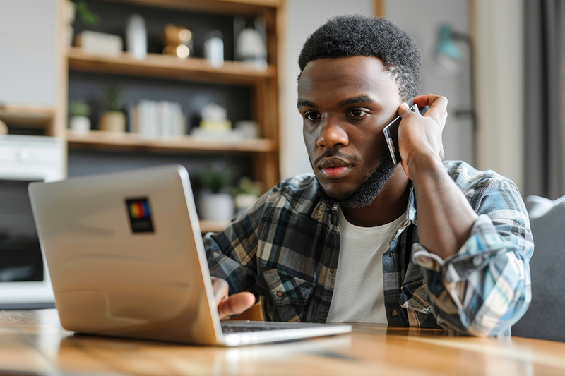 Man sitting at table on phone and computer looking frustrated