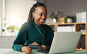 Smiling woman sitting at her laptop and holding a debit card