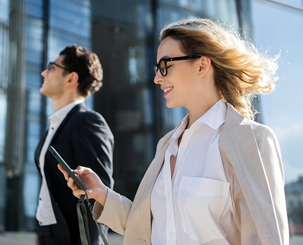 Two professional women in business attire standing outside a modern glass building, wearing glasses and holding documents
