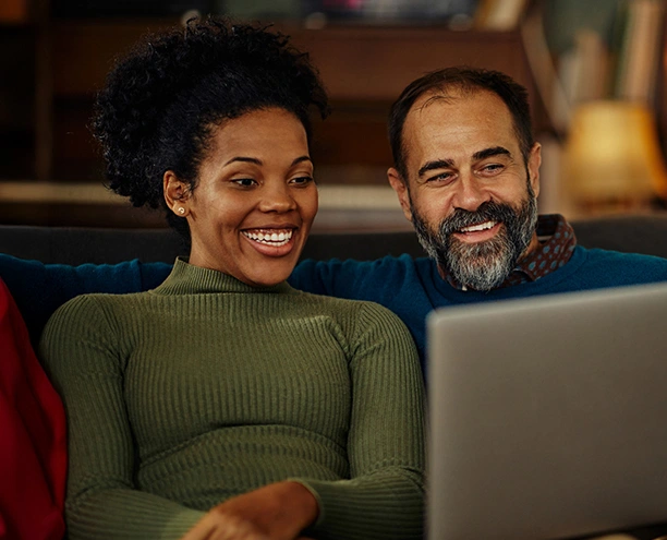 couple on couch looking at computer smiling