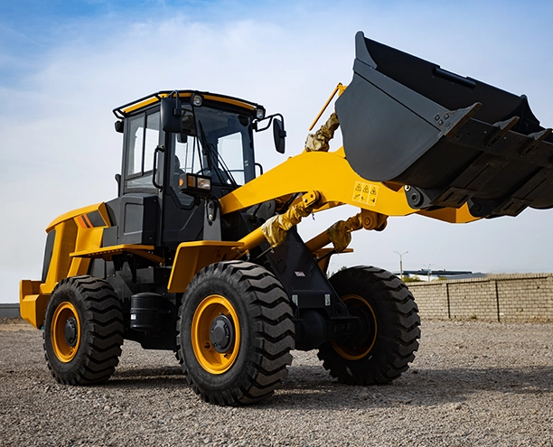 Yellow and black wheel loader with raised bucket attachment on gravel surface against clear sky