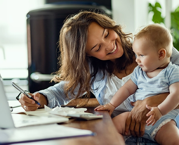 Woman smiling at baby on her lap while going over receipts