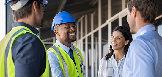 Four construction professionals in hard hats and safety vests converse outdoors.