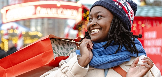 Woman smiling with a holiday shopping bag slung over her shoulder