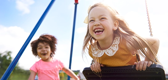 Close up of kids smiling enthusiastically swinging on a swing