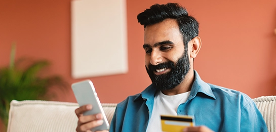 Man smiling with debit card in one hand, smartphone in the other hand