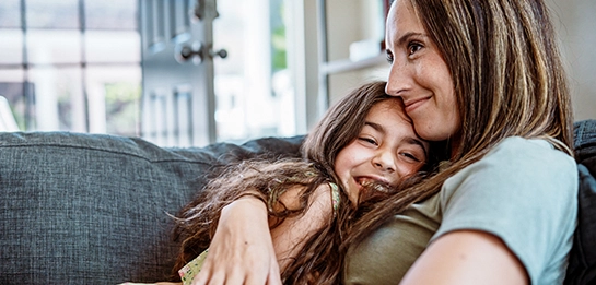 Woman snuggling with young girl, both smiling
