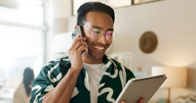 Man smiling, looking at a tablet, talking on a smartphone