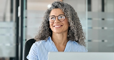 Woman sitting in front of a laptop gazing out the window smiling