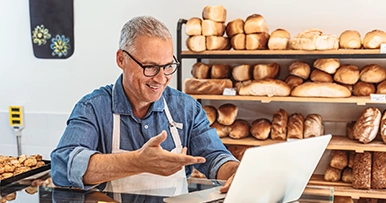 Senior entrepreneur smiling using a laptop in a bakery