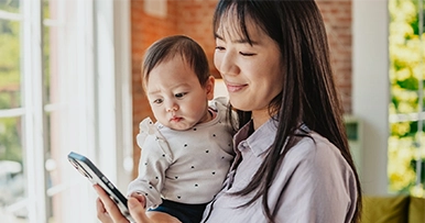 A mom holding her baby and looking at her phone