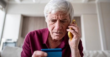senior man on a phone call reading his credit card looking confused