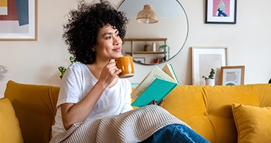 woman drinking coffee reading a book on her living room couch