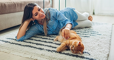 woman playing with her orange cat on the living room floor