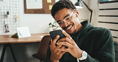 man laughing while holding a phone at his home office desk