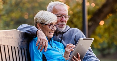 seniors sitting on a  park bench using a tablet device