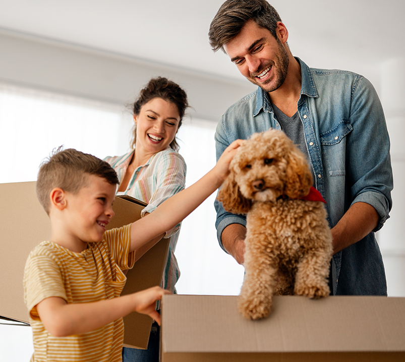 family with their dog unpacking boxes on moving day to new home