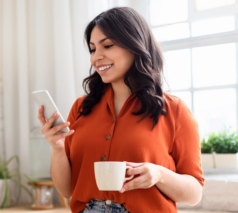 Woman holding a mug and looking at her mobile device
